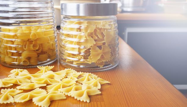 Pasta in the form of bows scattered from glass jar. Italian handmade pasta on the wooden background.