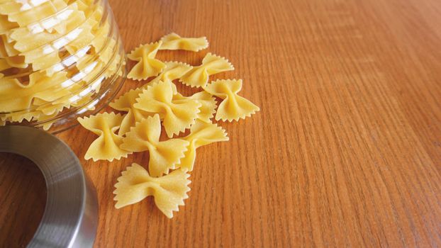 Pasta in the form of bows scattered from glass jar. Italian handmade pasta on the wooden background.