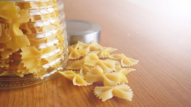 Pasta in the form of bows scattered from glass jar. Italian handmade pasta on the wooden background.