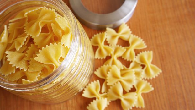 Pasta in the form of bows scattered from glass jar. Italian handmade pasta on the wooden background.