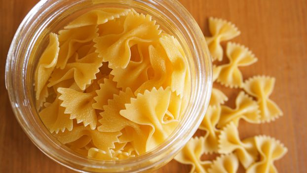 Pasta in the form of bows scattered from glass jar. Italian handmade pasta on the wooden background.