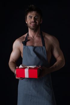 Handsome muscular naked man in an apron holding holiday gift box