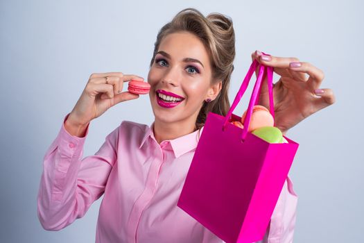 Funny smiling blond woman eating colorful macaroons