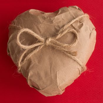 Heart in brown Wrapping Paper tied with rope bow on red background Valentine day surprise concept