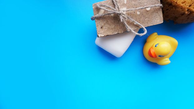 Gray and white Handmade soap and yellow toy duck on a blue background. Flat lay photo, top view