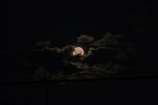 The moon behind clouds over a dark sky