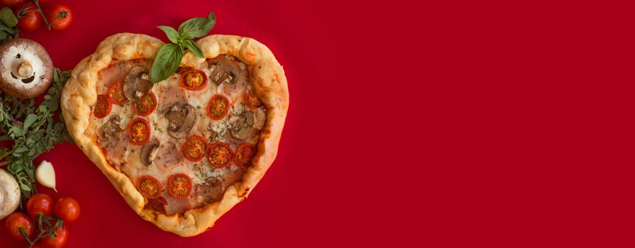 Pizza heart shaped with ham tomatoes and mushrooms on red background . Concept of romantic love for Valentines Day . Love food