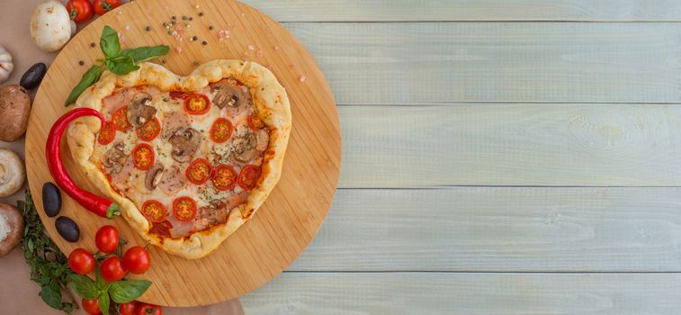 Pizza heart shaped with ham tomatoes and mushrooms on wooden background . Concept of romantic love for Valentines Day . Love food