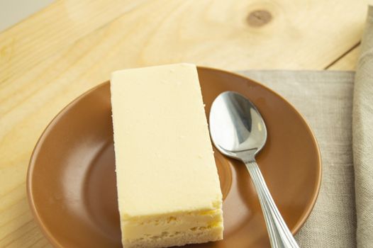 A piece of classic new York vanilla cheesecake on a light wooden background and linen napkin, close-up