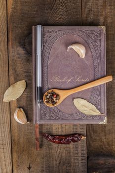 Book of Secrets broen closed cookbook on old wood background with spices