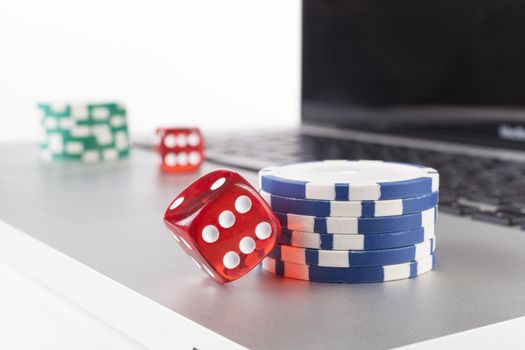 Red casino dices with chips on silver laptop isolated on white background