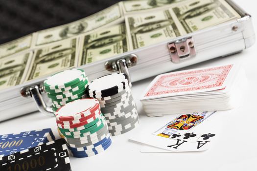 Casin ochips with briefcase full with dollars in the backgrouns and playing cards isolated on white