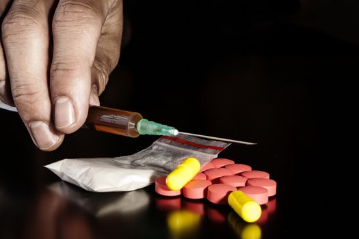 Hand holding syringe with powder and pills on black table with reflection