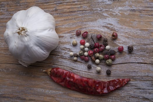Garlic red dry chily and various types of black pepper on wood background