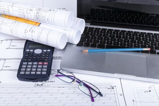 Architect blueprints with a calculator ans a silver laptop with pencil and glasses