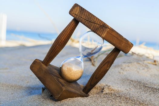 Old wooden houglass in sand on the beach with the sea and blue sky in the background