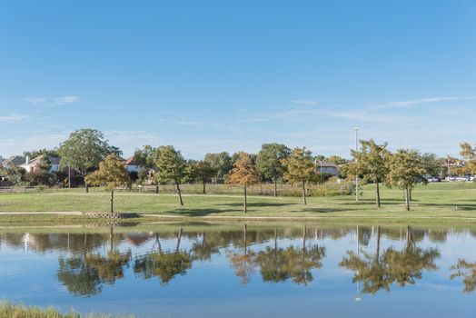 Lakeside residential area with single-family detached houses near natural park with pathway. Cloud blue sky reflection, suburb Dallas, Texas, USA