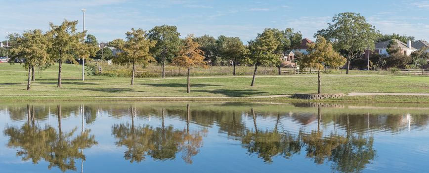 Panorama view lakeside residential area with single-family detached houses near natural park with pathway. Cloud blue sky reflection, suburb Dallas, Texas, USA