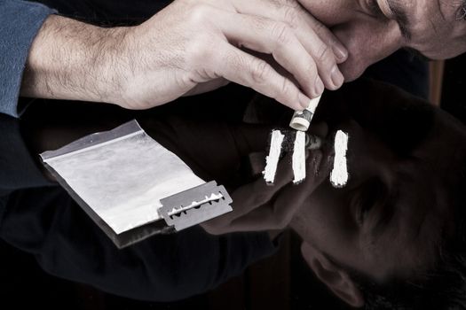 Man snorting white drug rows with rolled up dollar banknote on dark with reflection