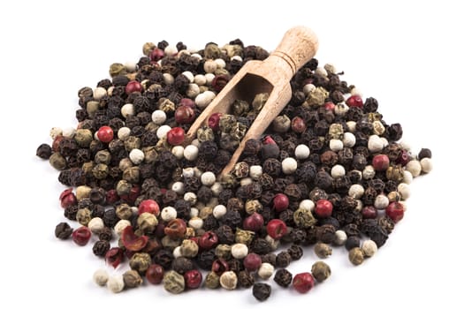 Dry coloured pepper types heap with wood spoon isolated on white background