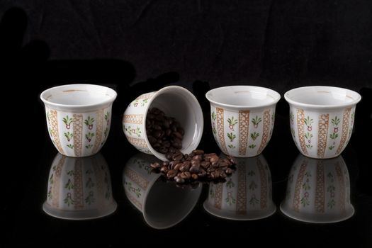 Hand painted traditional arabic coffee cups on black background and coffee beans with reflection