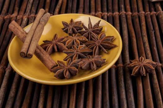 Cinnamon sticks with star shape anis on yellow plate and wood background