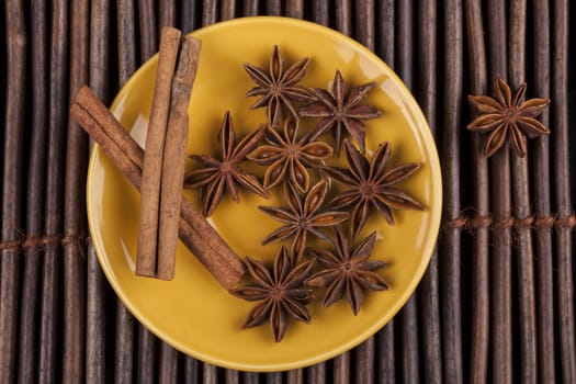 Cinnamon sticks with star shape anis on yellow plate and wood background