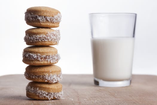 Coconut round cookies tower on wood plate with glass of milk in the background