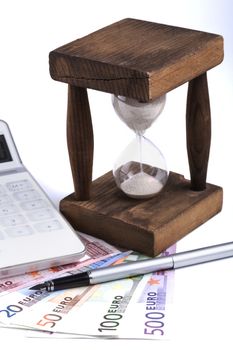 Different euro banknotes with hourglass white calculator and silver founten pen on white background