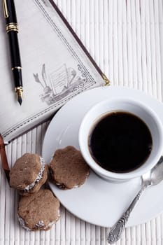 brown cookies with coffee in a white mug and silver spoon with fountainpen and old notebook on white wood background