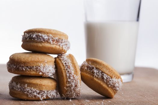 Small round cocnut cookies with  glass of milk in the bakcground on wooden plate