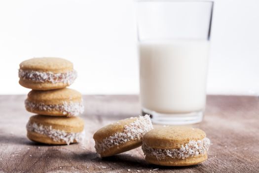 Small round cocnut cookies with milk glass in the bakcground on wooden plate