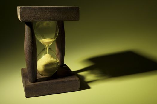 Old wooden hourglass with shadow in yellow light
