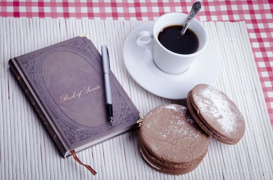 Old notbook closed with fountain pen round cookies and cup of coffee on white wood background