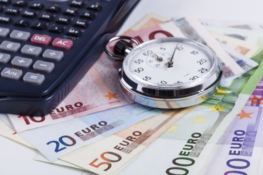 Euro banknotes on white background with black calculator and silver nalog stopwatch