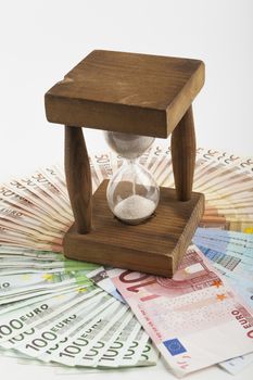 Old wooden Hourglass in the middle on euro banknotes circle