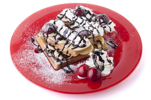Belgian waffle with chocolate syrup whipped cream and red cherry on red plate