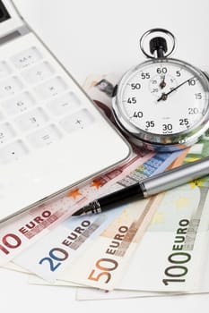 Euro banknotes on white background with white calculator and silver analog stopwatch and fountain pen