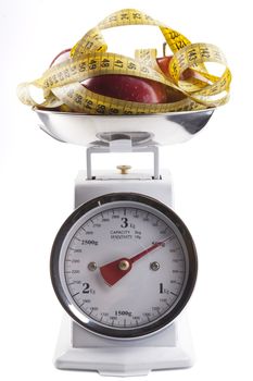 Red apple with  yellow measuring tape on kitchen scale isolated on white