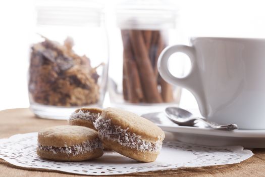 Small round cocnut cookies with white coffee mug in the bakcground on wooden plate