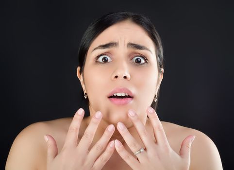 Beauty portrait of a girl with fingers near her face who looks at the camera with fear or surprise