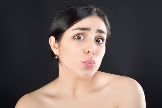 Beauty portrait of a girl with bare shoulders who shows off her lips sending a kiss to the camera. Studio shot on black background