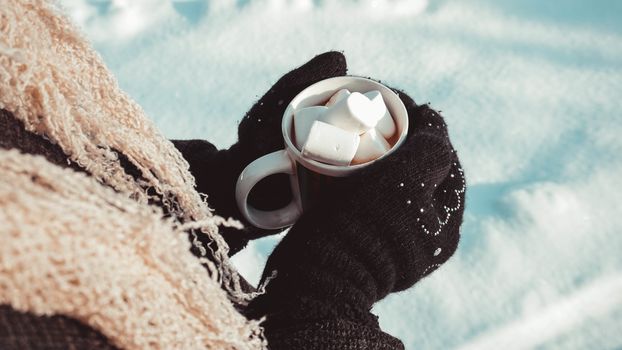 A cup of cocoa with marshmallows in hands in mittens. Warm winter background. Warming drink.