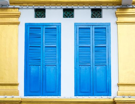 Beautiful facade detail with bright blue shutters on white and golden wall in Little India, Singapore