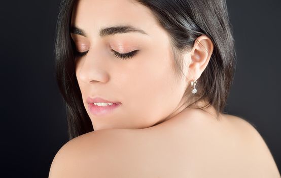 Portrait photo of a beautiful young brunette girl with her eyes closed who gets pleasure standing on a fern background in the Studio