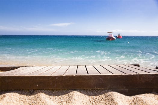 wooden plank in sand and blue sea in the background