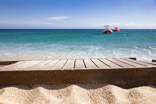 wooden plank in sand and blue sea in the background