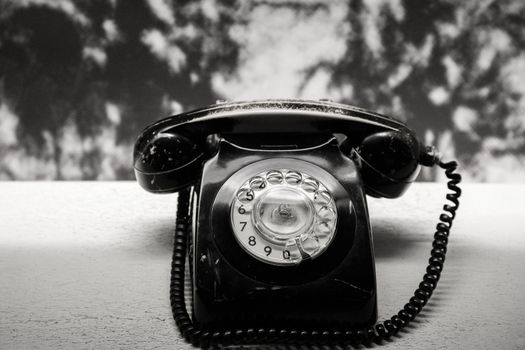 Retro rotary telephone on old table, black and white photo