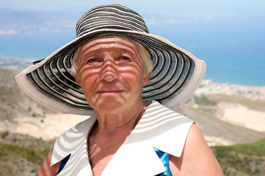 Happy elderly woman in sun-hat against the sea