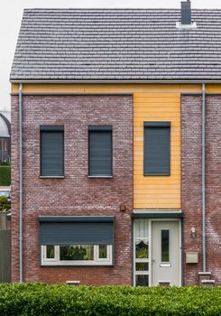 modern dutch terrace house decorated with plants behind the windows, some windows closed down with roller shutters, home in a dutch small village